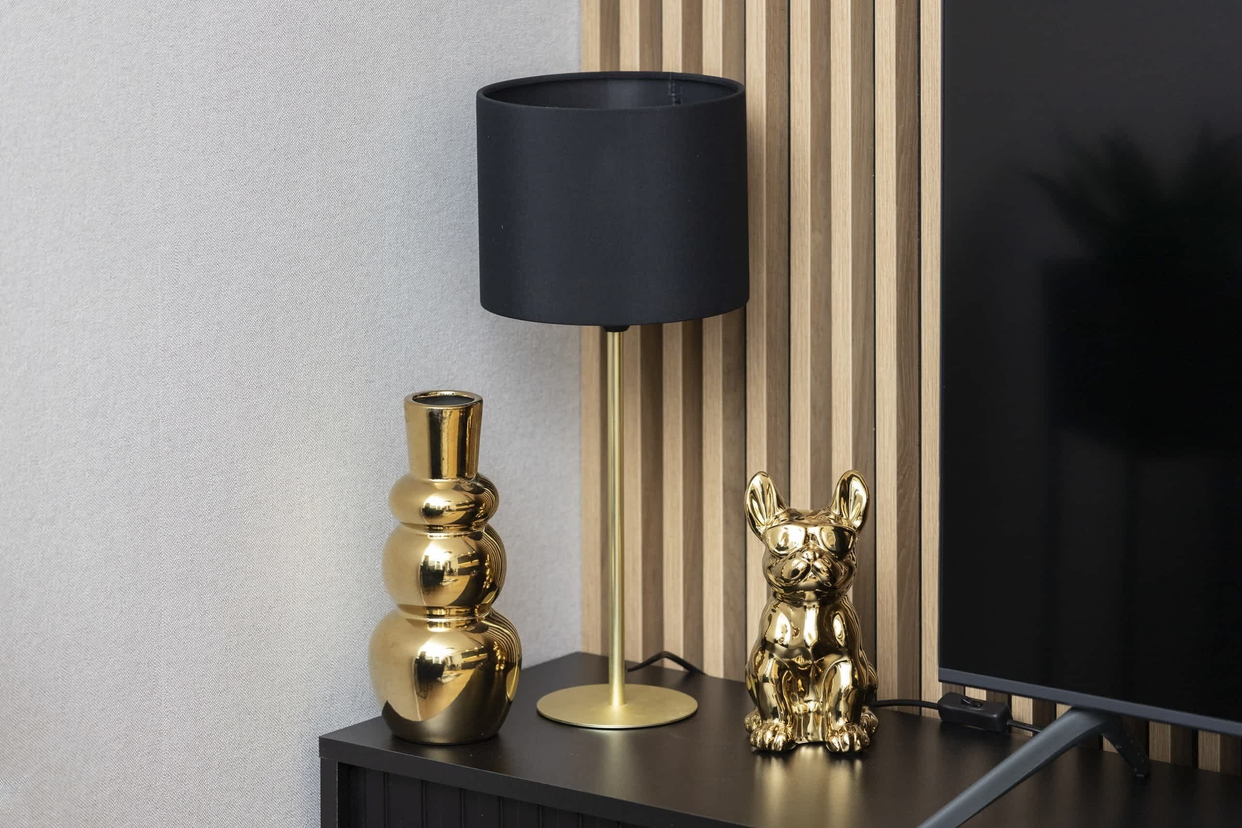 A modern interior with a black lamp, a gold vase, and a gold figurine on a dark console table.