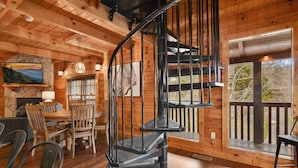 A wooden interior with a spiral staircase, a dining area, and a large window with a view of trees. - Grand Mtn Splash ~ Indoor Pool, Arcade, Theater & More! (Sevierville)