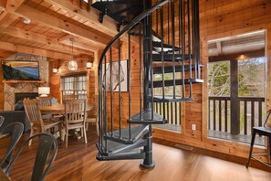 A wooden interior with a spiral staircase, a dining area, and a large window with a view of trees. - Grand Mtn Splash ~ Indoor Pool, Arcade, Theater & More! (Sevierville)