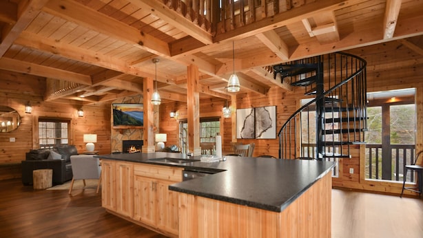 A wooden cabin interior with a kitchen island, dining area, and a spiral staircase. - Grand Mtn Splash ~ Indoor Pool, Arcade, Theater & More! (Sevierville)