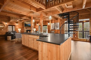 A wooden cabin interior with a kitchen island, dining area, and a spiral staircase.