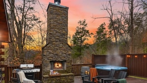 An outdoor patio with a stone fireplace, a hot tub, and outdoor seating. - Grand Mtn Splash ~ Indoor Pool, Arcade, Theater & More! (Sevierville)