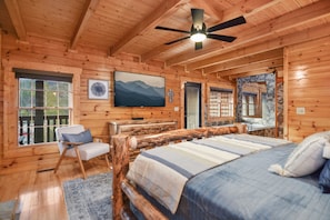 A log cabin bedroom with a bed, a chair, a television, and a window.