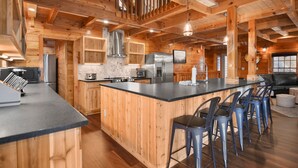A spacious kitchen with wooden walls, a large island with bar stools, stainless steel appliances, and a hanging light fixture. - Grand Mtn Splash ~ Indoor Pool, Arcade, Theater & More! (Sevierville)