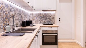 A kitchen with white cabinets, a stainless steel sink, a built-in oven, and a backsplash with blue and white tiles. - Casa Moderna - Two Bedroom Apartment (Corfu)