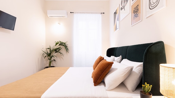 A neatly arranged bedroom with a bed, a potted plant, a wall-mounted TV, and framed artwork. - Casa Moderna - Two Bedroom Apartment (Corfu)
