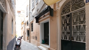 A narrow street with a parked scooter, a building with a decorative metal gate, and a small step leading to a door. - Casa Moderna - Two Bedroom Apartment (Corfu)