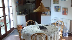 Un coin repas avec une table ronde, quatre chaises, un luminaire suspendu et une cuisine en arrière-plan.