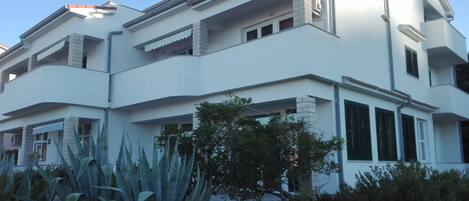 A modern two-story building with balconies, large windows, and a well-maintained garden with agave plants.