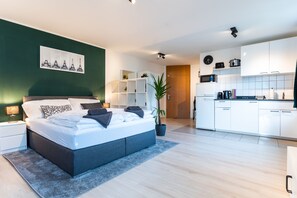 A modern bedroom with a large bed, a bedside table, and a nightstand. There is a small desk with a chair in the corner. The room has white walls and a green accent wall. - For our english speaking Guests (Böblingen)