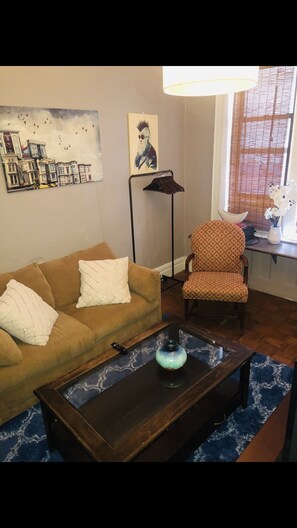 Relax in this inviting living space with a sofa, armchair, and coffee table, surrounded by a cityscape painting and a floor lamp.