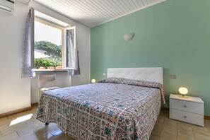 Une chambre à coucher avec un lit, une table de chevet, une fenêtre et une vue sur la verdure.