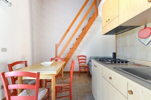 Keittiössä on puinen pöytä, punaiset tuolit, liesi ja puinen portaikko.