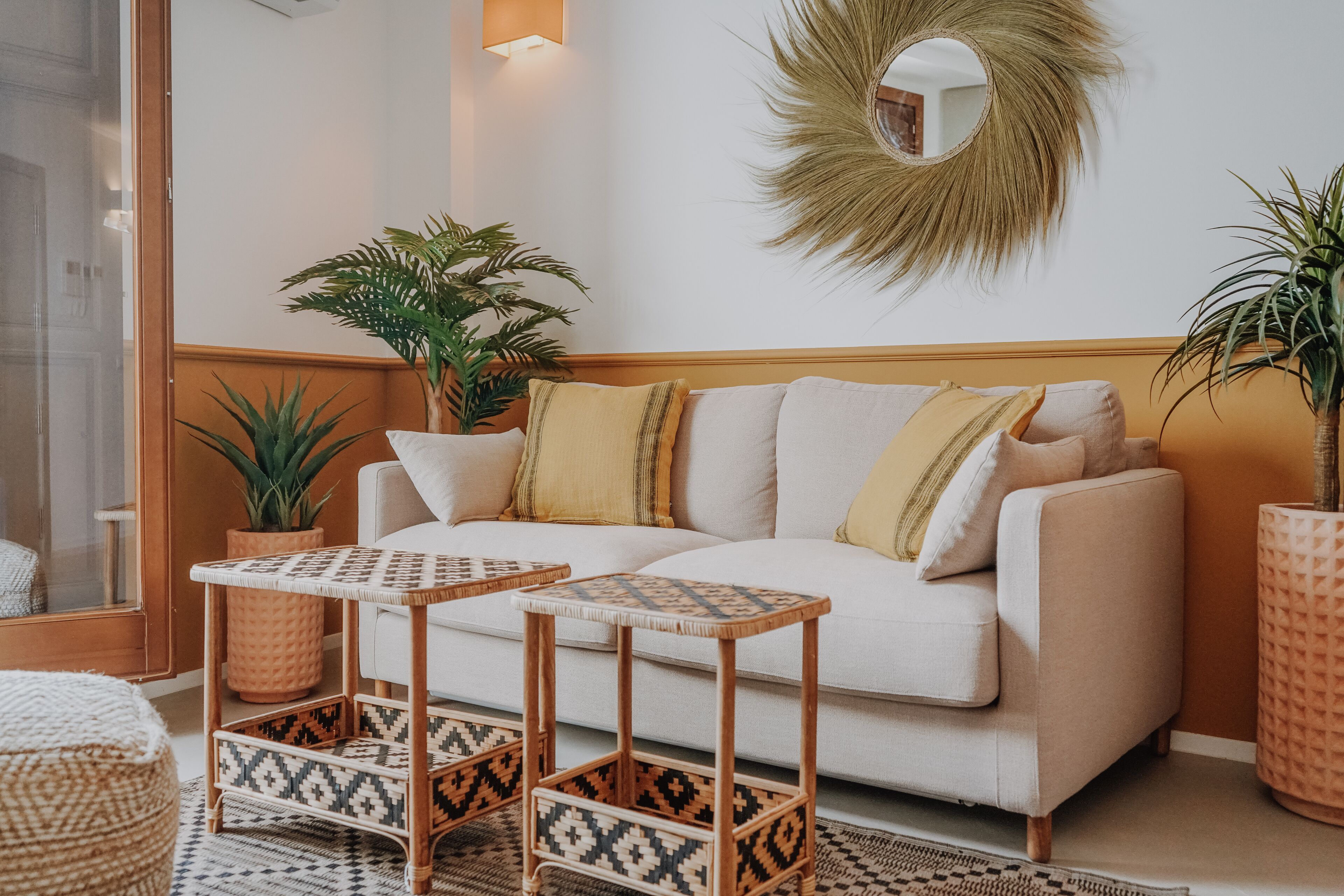 Un salón con un sofá blanco, dos mesitas de madera y varias plantas en macetas.