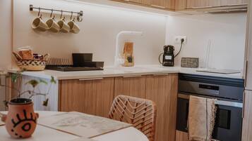 Una cocina moderna con armarios de madera, encimera blanca, un colgador para tazas, una cafetera y un reloj que marca las 12:39.