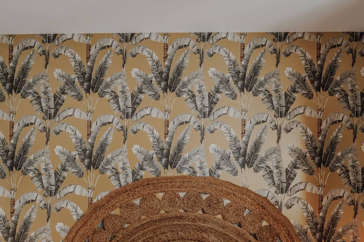 Un lit avec une tête de lit en osier, une literie blanche et un mur orné d’un motif de plumes.