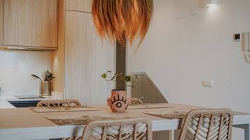 A modern kitchen with wooden cabinets, a laptop, a vase with a plant, and wicker chairs around a table.