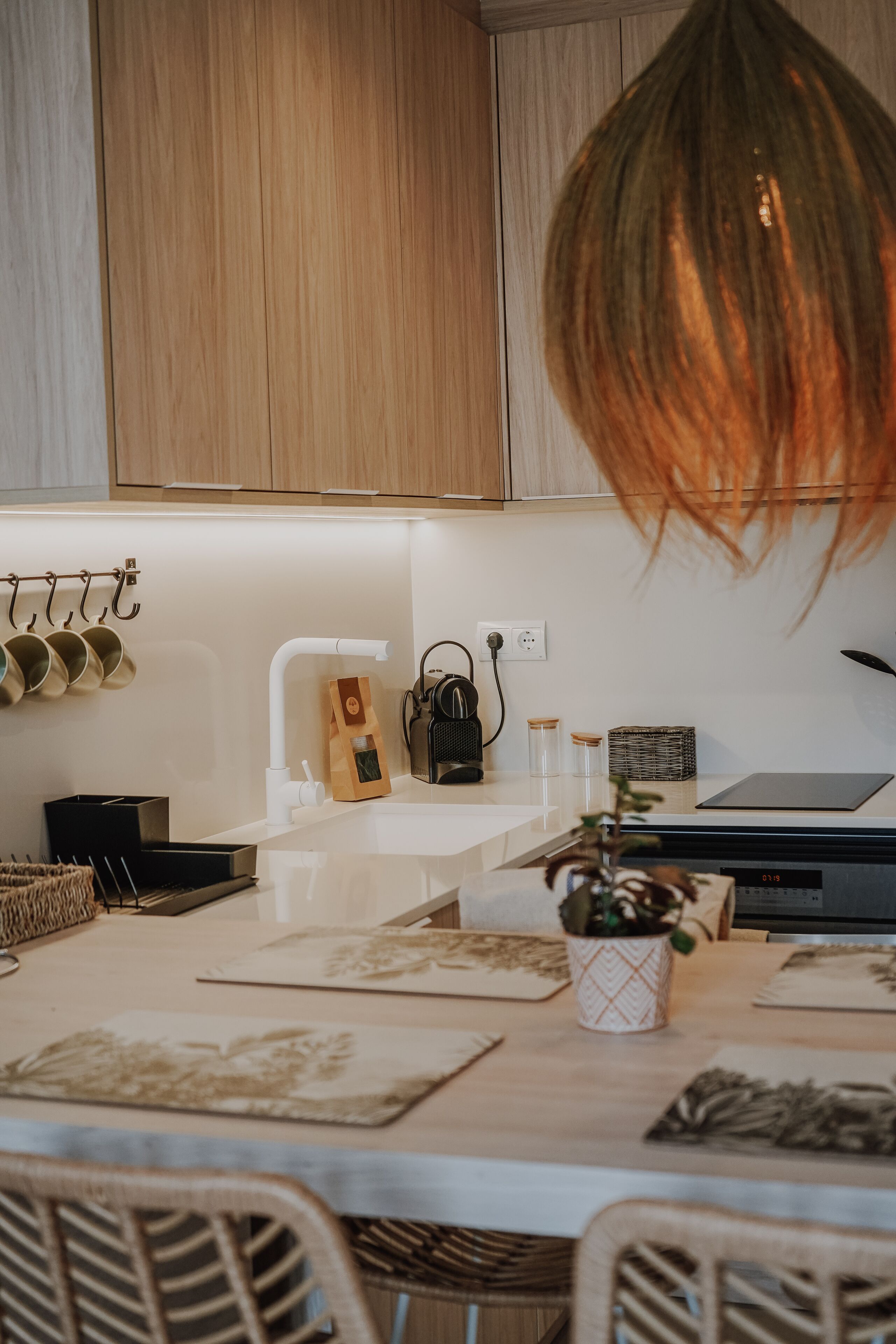 Una cocina moderna con armarios de madera, encimera blanca y un colgador para ollas.