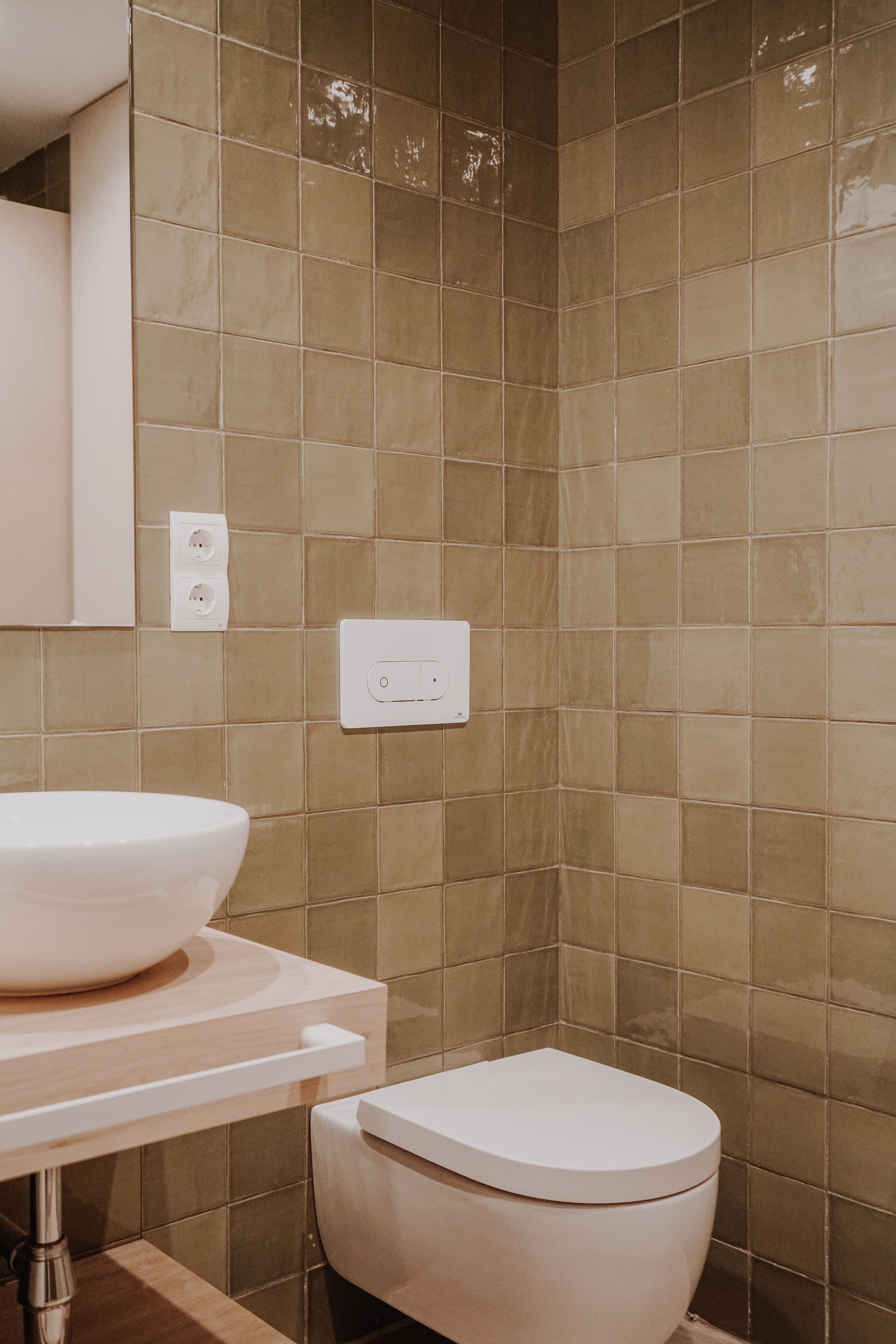 A bathroom with a beige tiled wall, a white sink with a large basin, and a white toilet.