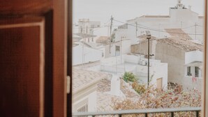 Vista a través de una puerta de madera de una zona residencial con edificios blancos y una vista distante del mar.