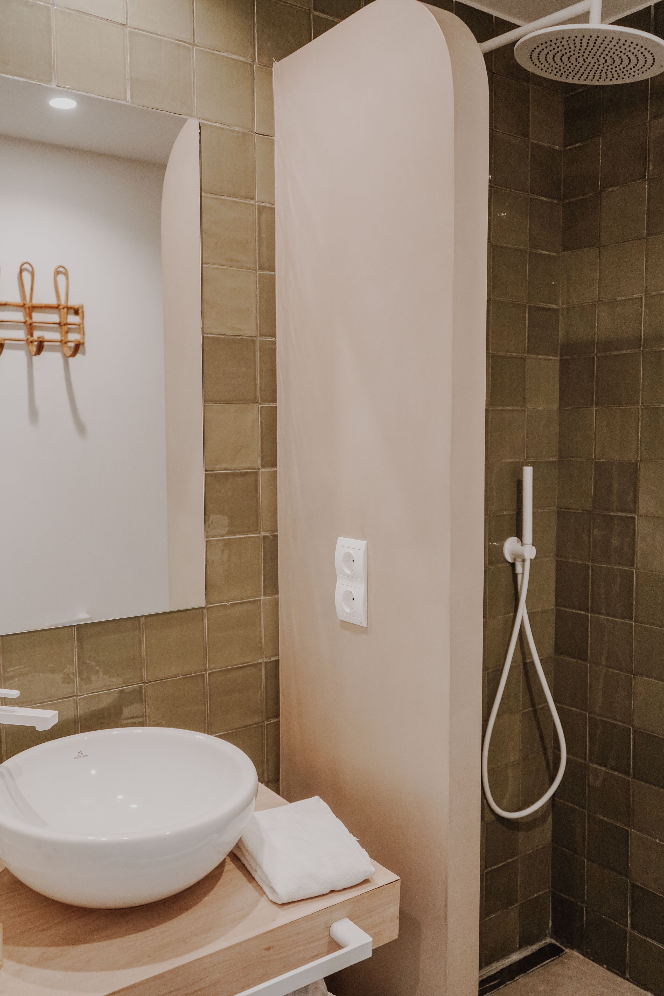 A bathroom with a white sink, a mirror, and a shower area with a handheld showerhead.