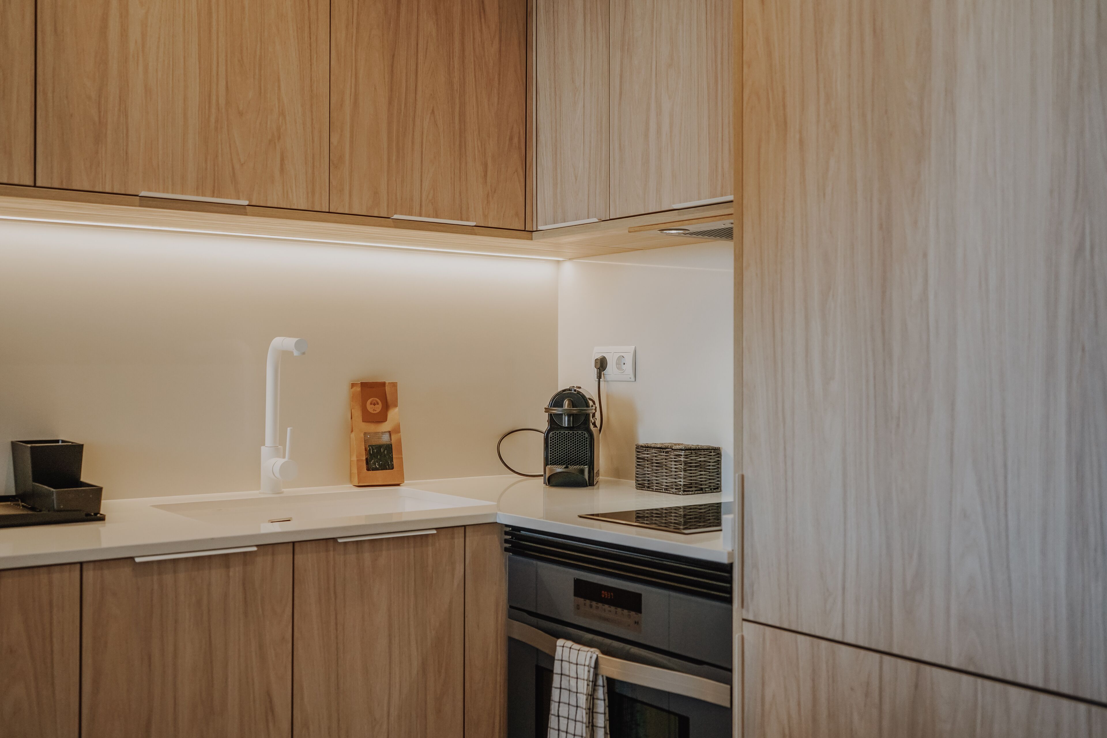 Una cocina moderna con armarios de madera, encimera blanca, cafetera y horno empotrado.
