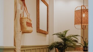 Un pasillo con un estante de madera que sostiene un bolso tejido, un espejo y una planta en maceta.