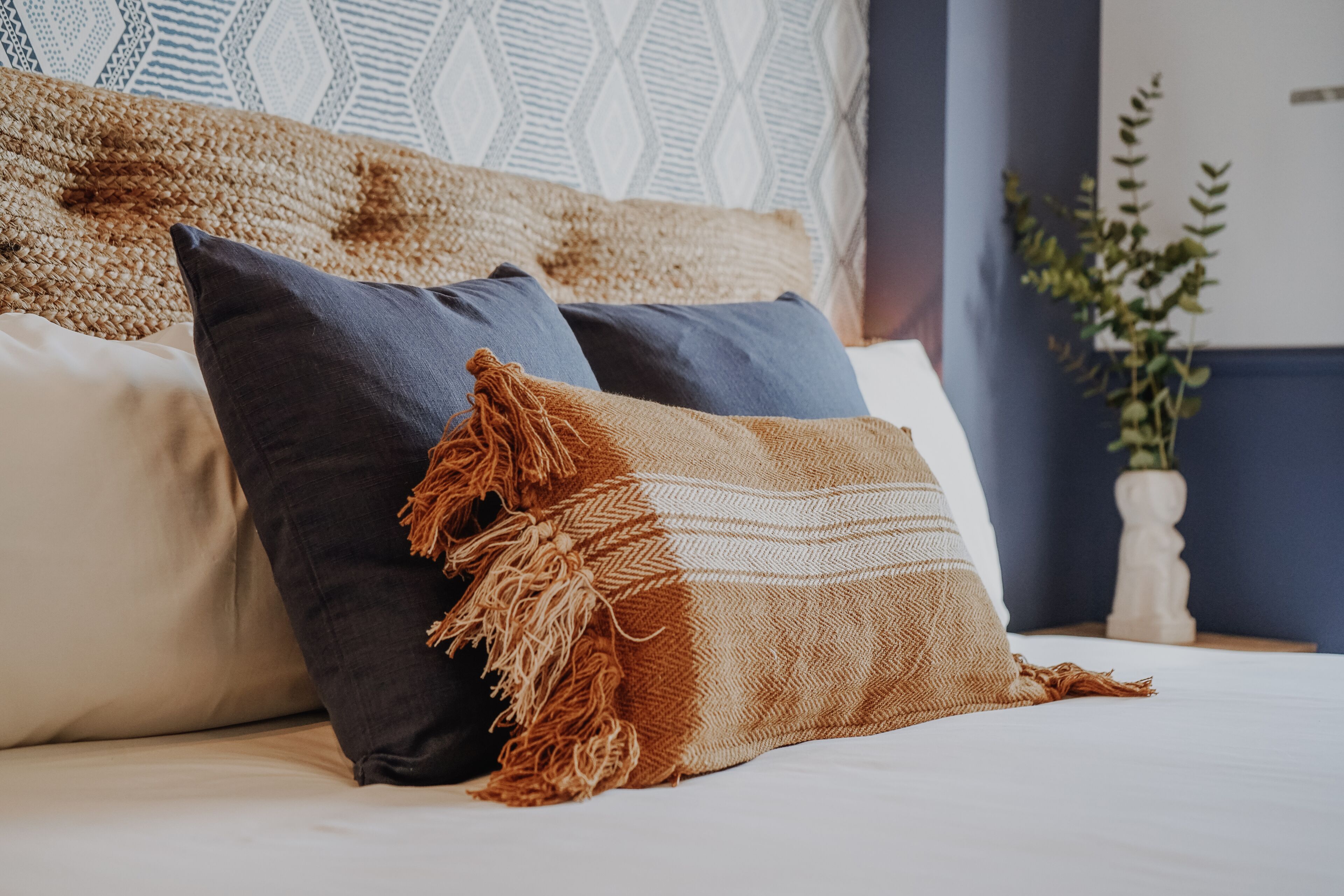 Una cama con tres almohadas, una manta tejida y un adorno en la pared.
