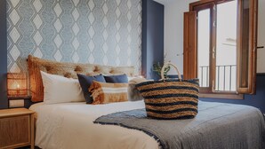 Una cama bien hecha con un bolso a rayas, un pared con diseño y una ventana con vistas.