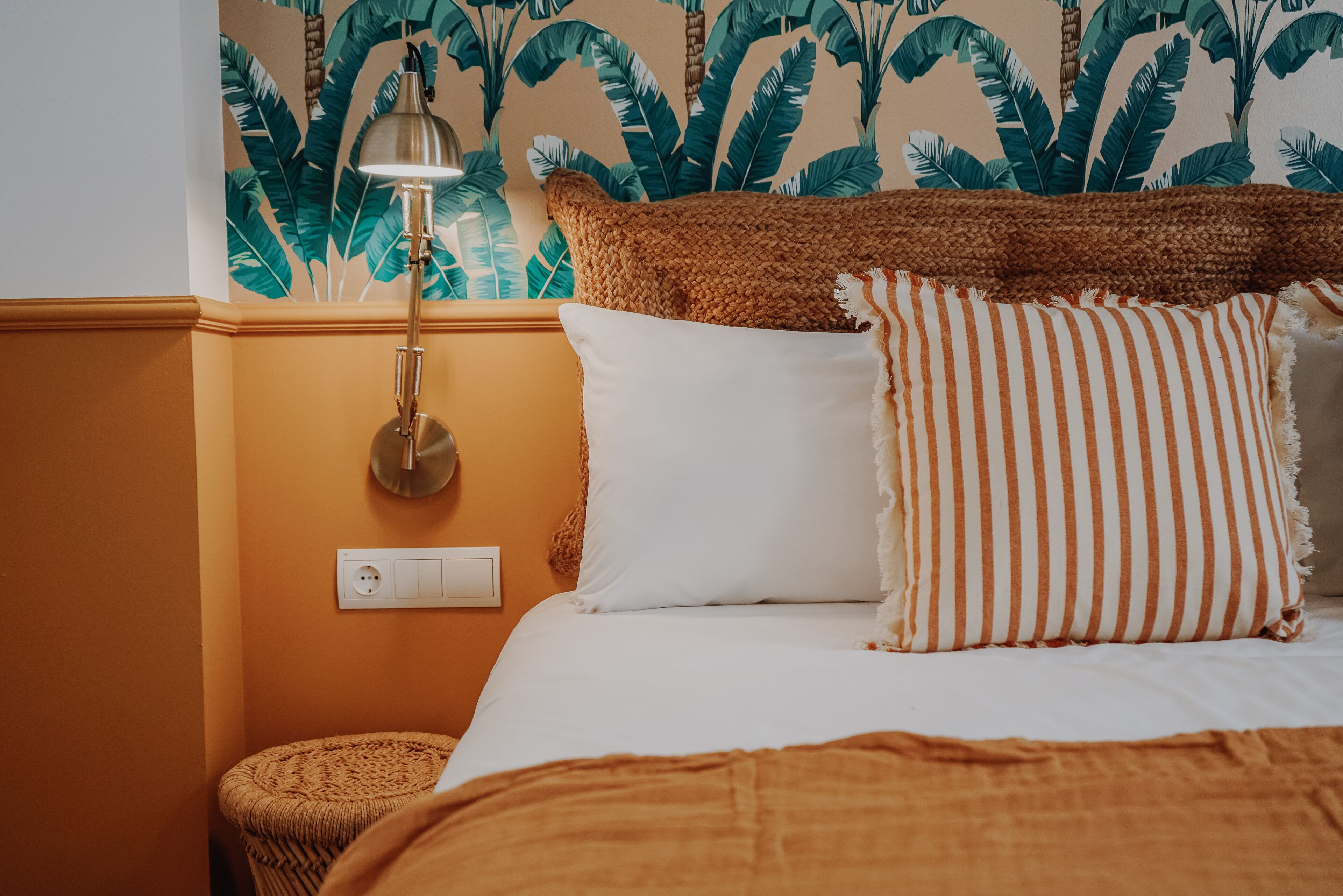 Een slaapkamer met een bed, een lamp, een stopcontact en een gestructureerde muur.
