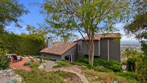 A modern house with a red-tiled roof, surrounded by lush greenery and a view of the city. - Stunning Panoramic Views From Contemporary Riviera Home! (Santa Barbara)