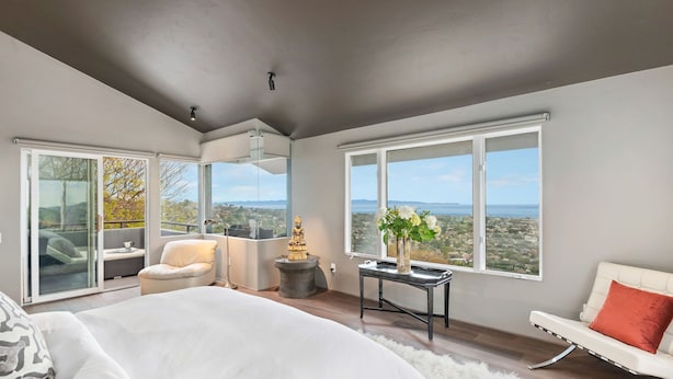 A modern bedroom with a large bed, a white sofa, a small table with a vase, and a statue. - Stunning Panoramic Views From Contemporary Riviera Home! (Santa Barbara)