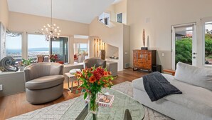 A spacious living area with a modern chandelier, a sofa, a glass coffee table, and a view of the outdoors. - Stunning Panoramic Views From Contemporary Riviera Home! (Santa Barbara)