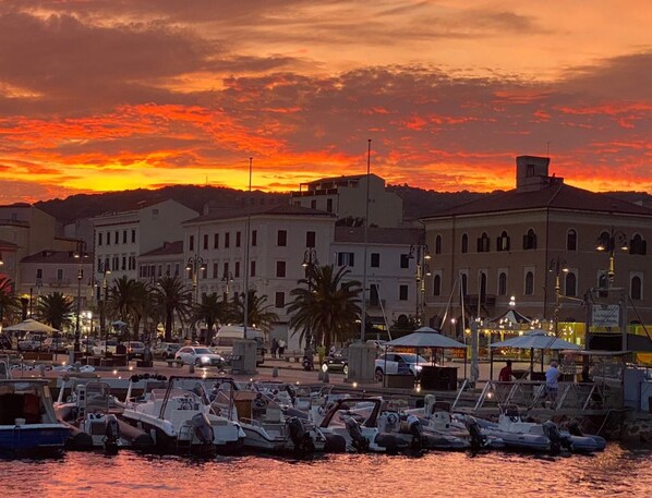 Un port de plaisance avec des bateaux amarrés, des bâtiments à l’architecture classique et un ciel au coucher du soleil.