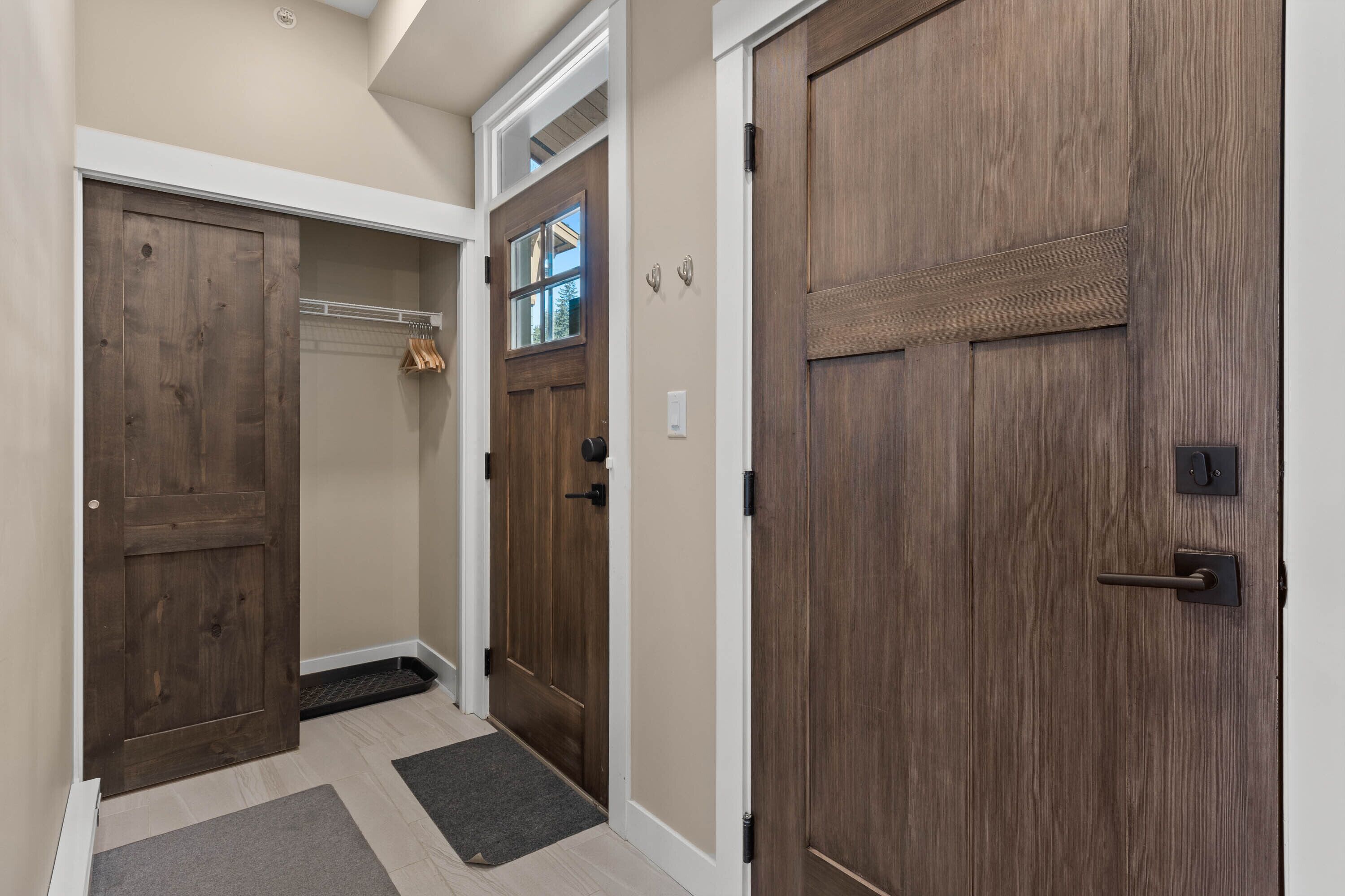 Un couloir avec deux portes en bois, un porte-manteau et une petite fenêtre.