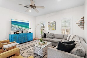 A living room with a sofa, a coffee table, a TV, and a blue cabinet. - Magnolia By The Sea, Heated Community Pool, 3 Bikes, 4 Minute Walk to Private Beach - BeachWalk (Panama City Beach)