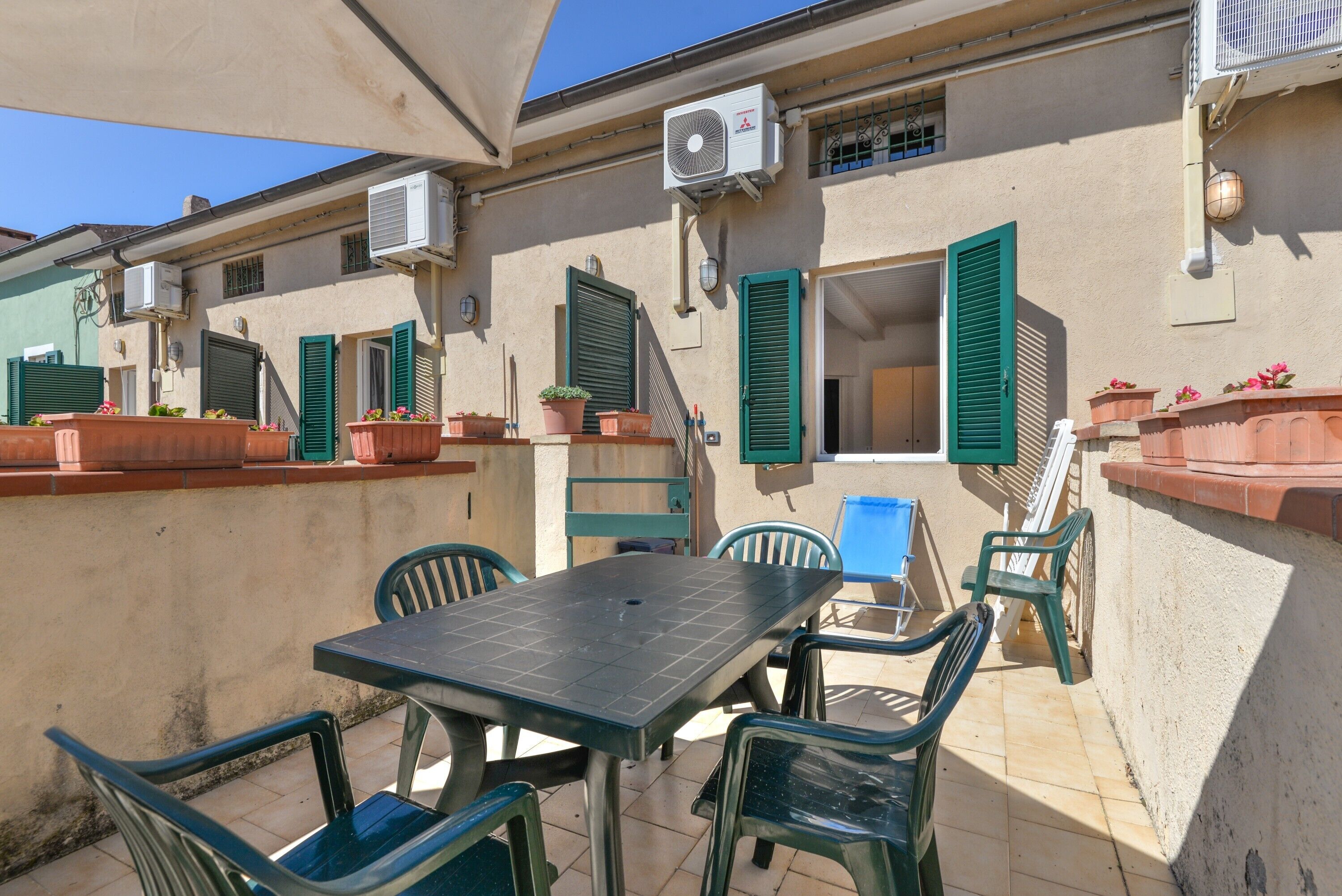 Une terrasse extérieure avec une table et des chaises, des unités de climatisation et des plantes en pot.
