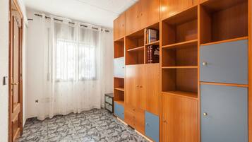 Quarto com guarda-roupa de madeira, janela com cortinas brancas e chão ladrilhado.