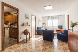Un salon comprenant un canapé, un téléviseur et un coin repas avec des meubles de rangement en bois et une cuisine.