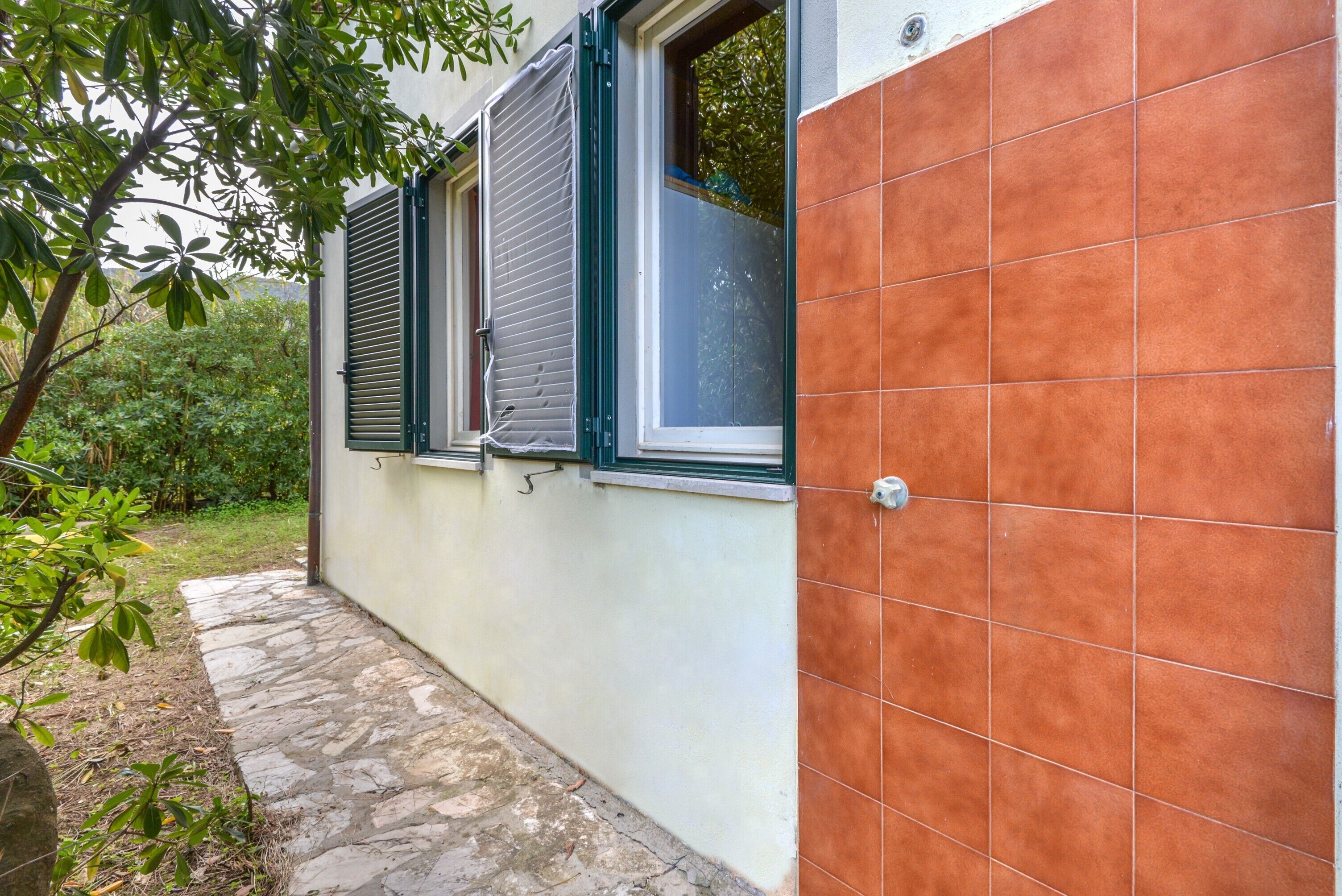 A building with a stone pathway, a window with shutters, and a tiled wall.