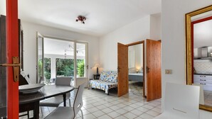 A room with a dining table, chairs, a sofa, and a bed. There is a door leading to another room.