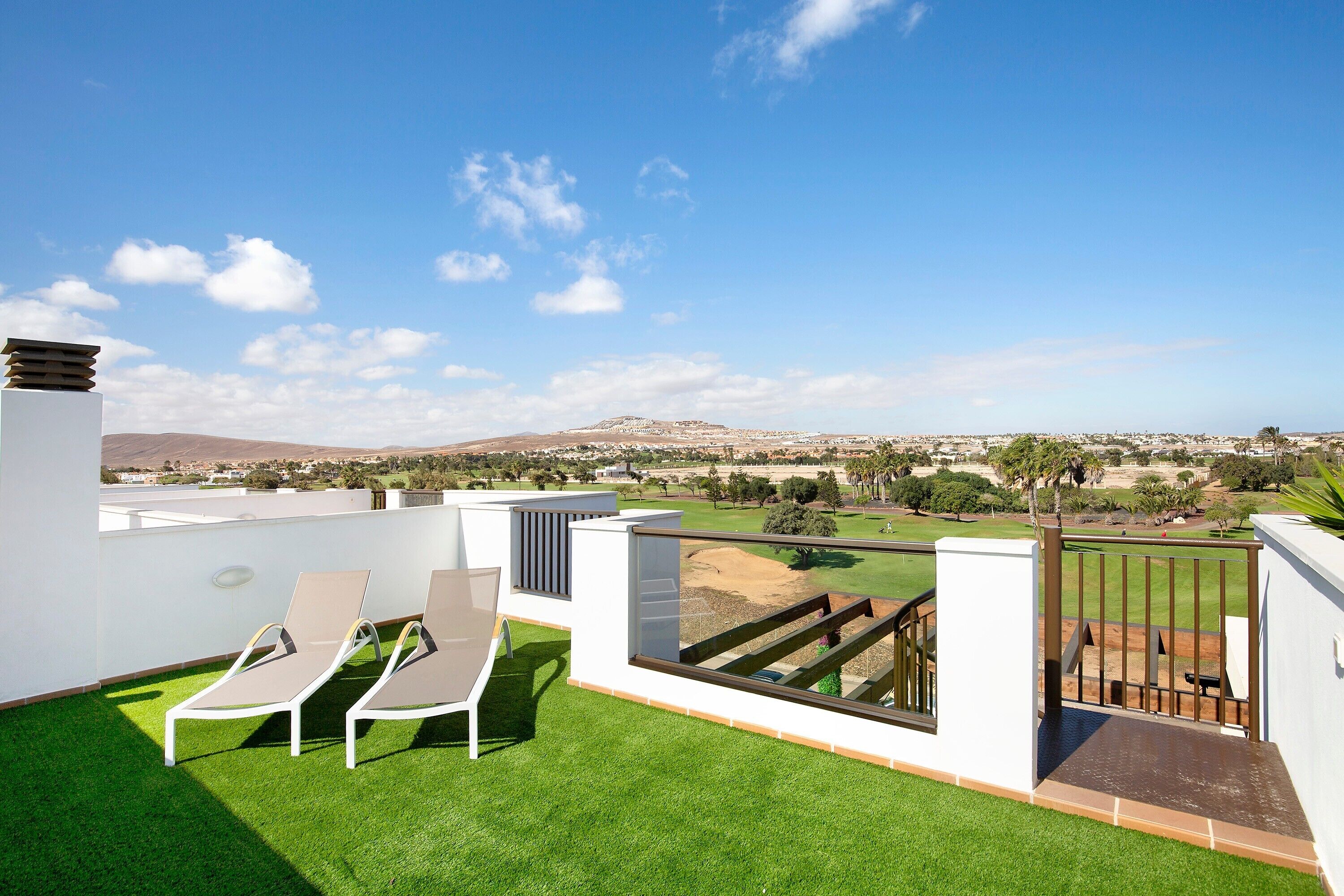 Ein Balkon mit zwei Lounge-Stühlen und Blick auf einen Golfplatz sowie ein fernes Gebirge.