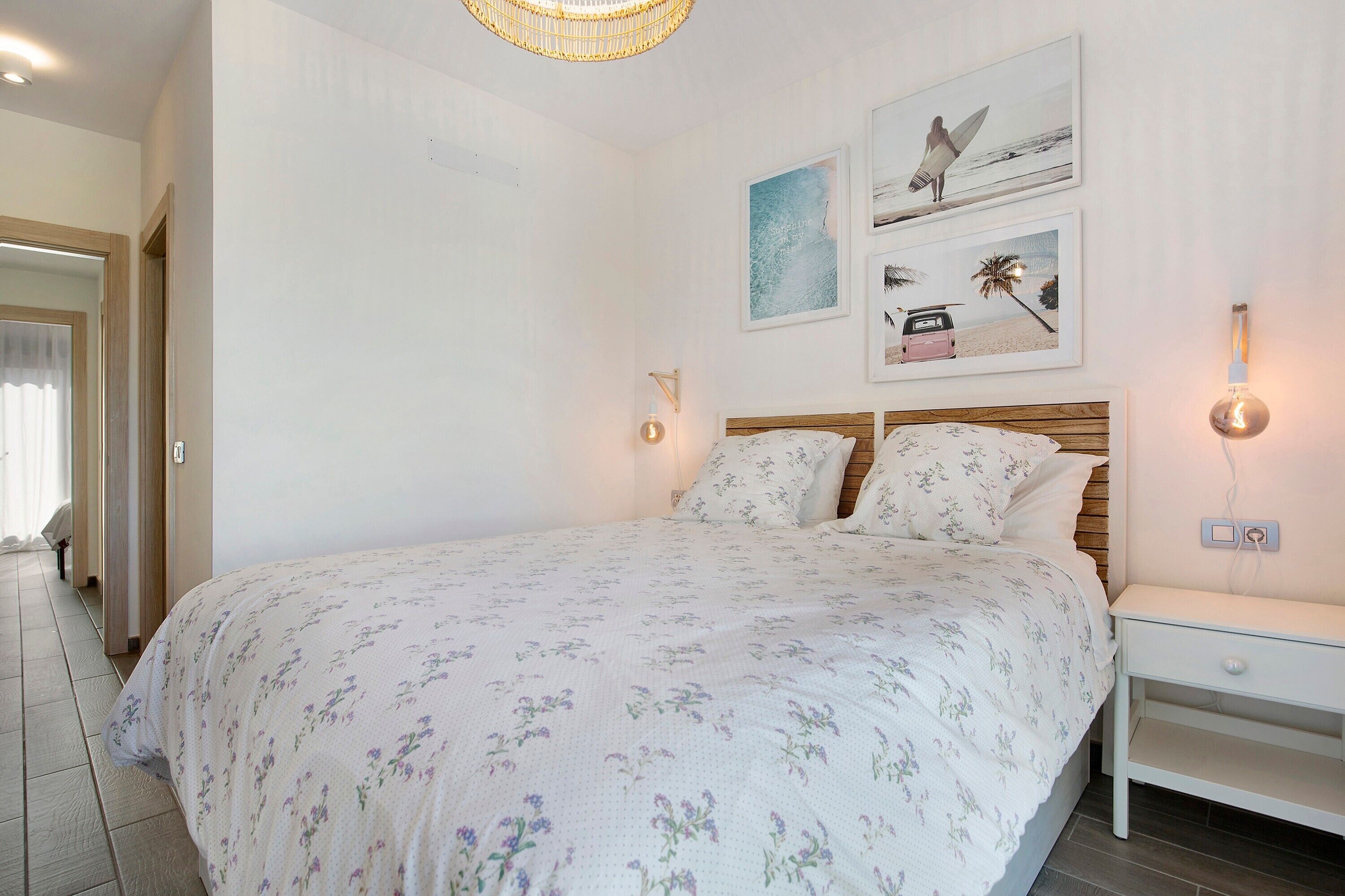 A bedroom with a bed, a nightstand, wall-mounted lights, and framed pictures.