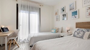 Ein Hotelzimmer mit zwei Betten, einem Schreibtisch, einem Stuhl, einem Laptop, einem Nachttisch mit Lampe und Wandbildern.