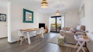 Ein modernes Wohnzimmer mit Essbereich, einer Couch, einem Fernseher und Blick auf einen Balkon.