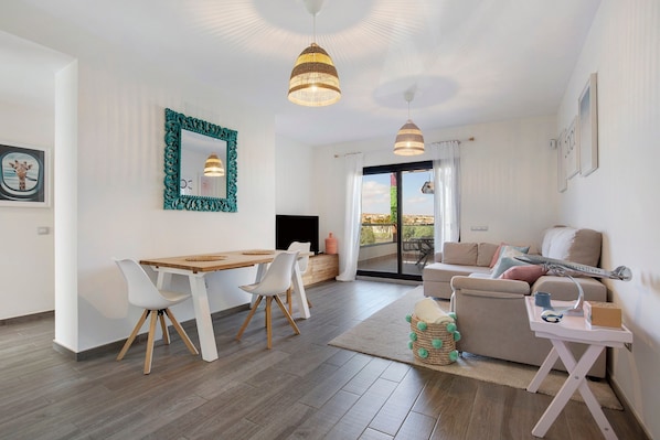 A modern living room with a dining area, a sofa, a TV, and a balcony view.