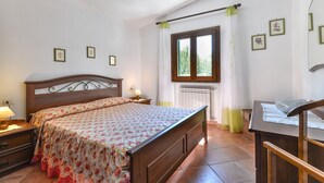 Une chambre à coucher avec un lit en bois, une table de chevet avec une lampe, une commode, une fenêtre avec des rideaux et des tableaux encadrés accrochés au mur.