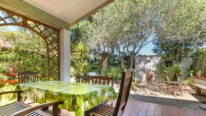 Une terrasse extérieure avec une table et des chaises, entourée de plantes et d’arbres.