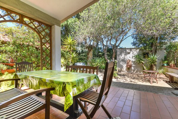 Une terrasse extérieure avec une table et des chaises, entourée de plantes et d’arbres.