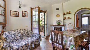 Une pièce comprenant un canapé à motifs floraux, une table à manger en bois, des chaises, un coin cuisine et une porte donnant sur l’extérieur.